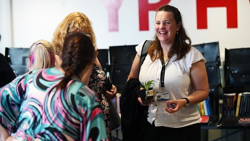 Tutors laughing with each other, one holding a plant from a plant swap, laughing together
