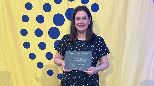 Lisa standing up with the Coleg Cenedlaethol branding in the back holding her award