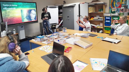Ace in a classroom with people listening around tables