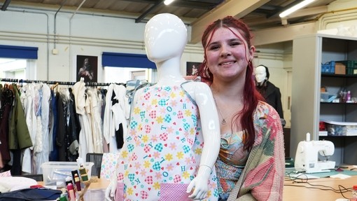A student holding up her completed dress on a child mannequin