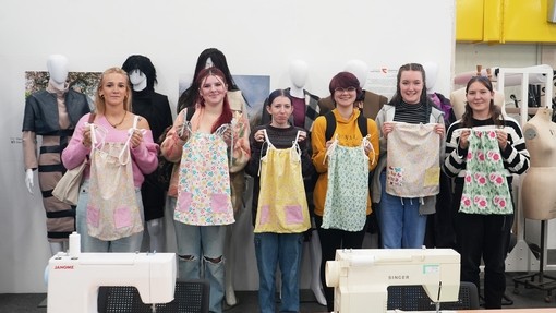 The group of students lined up each showing their garment on a child mannequin