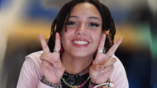 Ace looking at the camera from a desk doing a finger peace sign