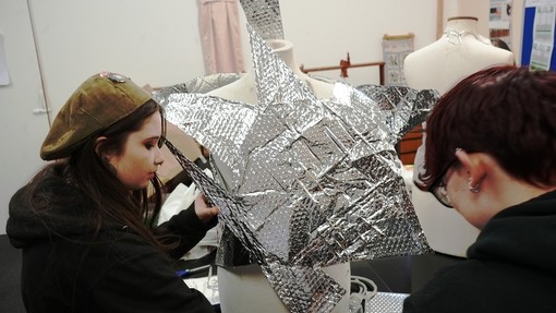 Two students working with silver material on a mannequin
