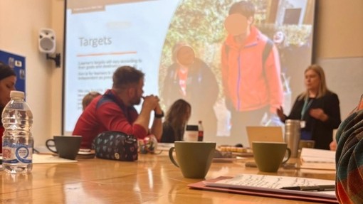 PGCE students at desks at Coleg Elidyr with a screen behind and someone talking