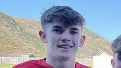 Sion wearing a red top, a headshot in front of some mountains