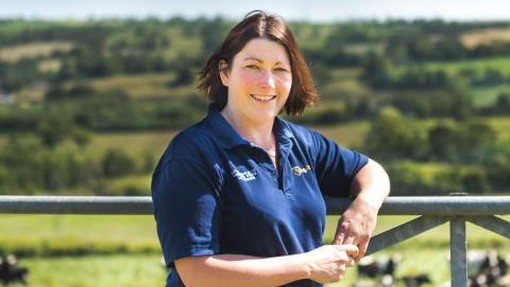 Liz standing and leaning on a fence outside with grassland behind her looking at the camera