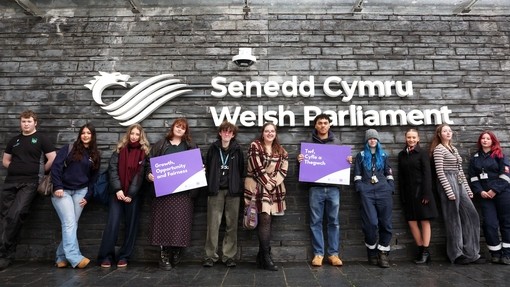 Students outside the Gwersyll yr Urdd building holding up a sign saying, growth, opportunity, fairness