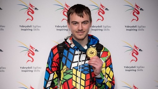 A student wearing a rubix cube themed suit holding a gold medal 