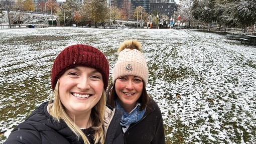 Two members of staff in a snowy field in hats looking at the camera