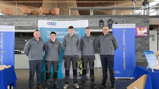 Students at the Senedd in their branded grey jackets with lecturers Rhodri and Huw