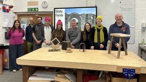 Students in a row with their prototypes in the workshop by a bench