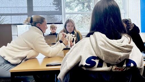 The vet physio leaning over a desk explaining some anatomy to students