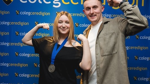 Student with her medal and tutor doing a strong man pose