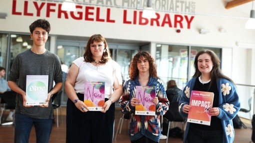 Four members of the team in a row each holding and edition of the magazine they are in Starbucks