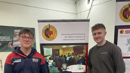 Celt and Owain standing next to a branded Guild of Bricklayers stand