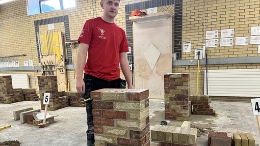 A student in a red t-shirt standing by his finished brickwork construction