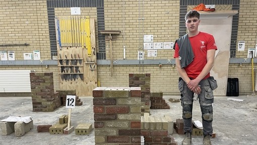 A student in a red t-shirt standing by his finished brickwork construction