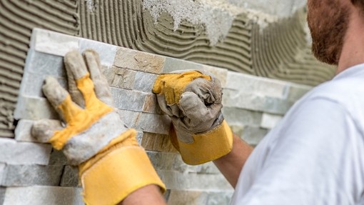 Image of a young man in yellow gloves tiling a wall