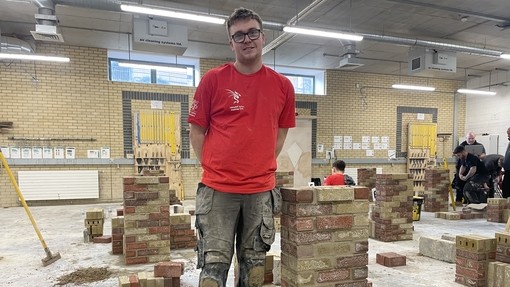 A student in a red t-shirt standing by his finished brickwork construction