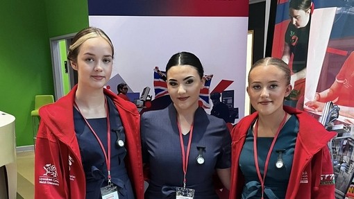 Three competitors in uniform and with Wales hoodies with skills branding behind