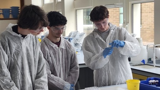 Three students conducting an experiment wearing PPE and lab coats 