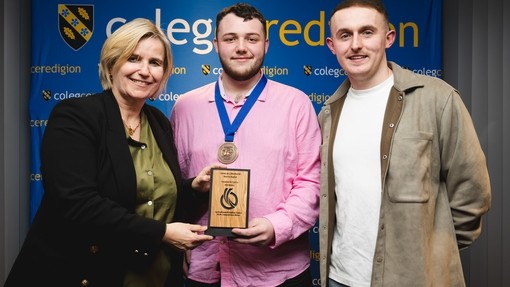 Acting principal Vanessa with Glyn and tutor Sam college branding behind Glyn holding skills competition Wales medal