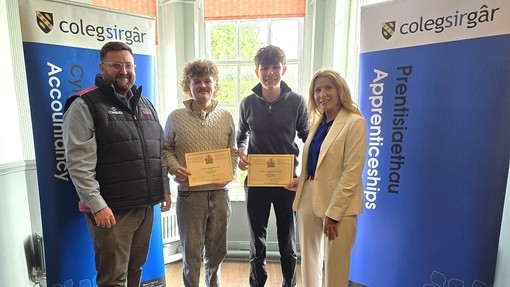 The two apprentices standing with Gareth David and a rep from the Worshipful Livery with two college branded banners on each side (they are holding certificates)