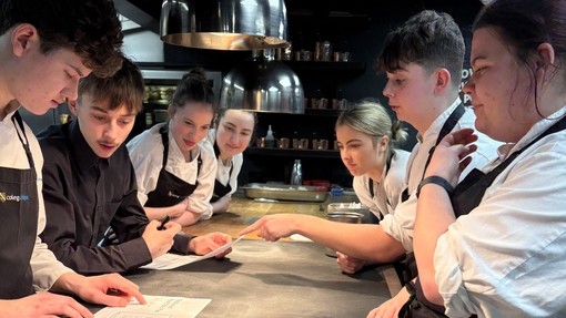 Students in the kitchen discussing arrangements over a table, hospitality and catering they are all in uniform