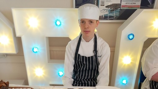A catering student in uniform with home made cakes by a table