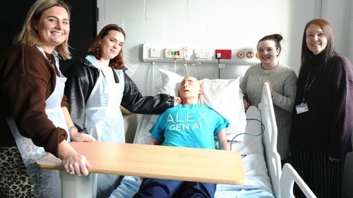 Alex the AI mannequin in a bed with a student and lecturer one side and the other Rebecca and Vicky