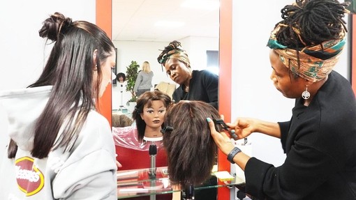 Edwina working on an afro mannequin head with an onlooking student