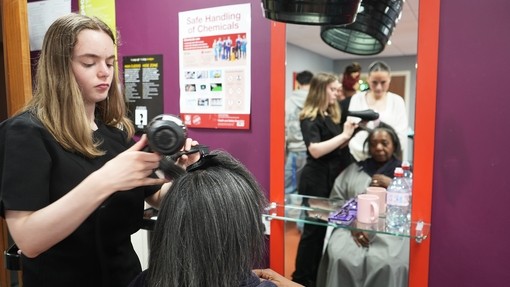 A student blow drying afro hair in a client session
