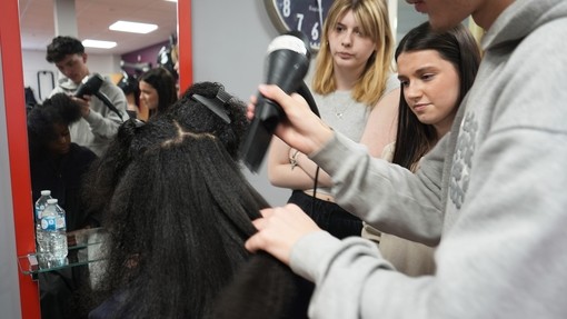 A student working with afro hair in a client session with onlooking students