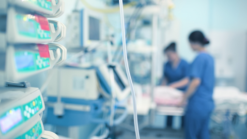 Foreground a medical machine and background blurred nurses seeing to a patient