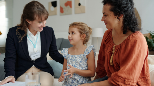 An official with lanyard, child in the middle and mum to the right, in a house visiting setting