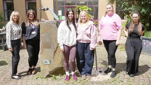 A row of students standing looking at the camera in the garden with a statue of two hands touching