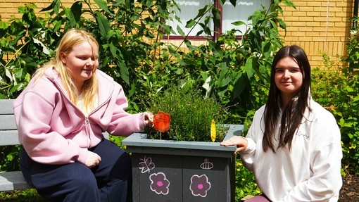 two students crouched in the garden by a potted plant