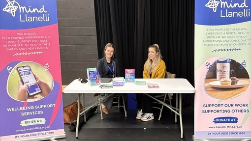 Two people from Mind Llanelli sitting on a table with branded stands