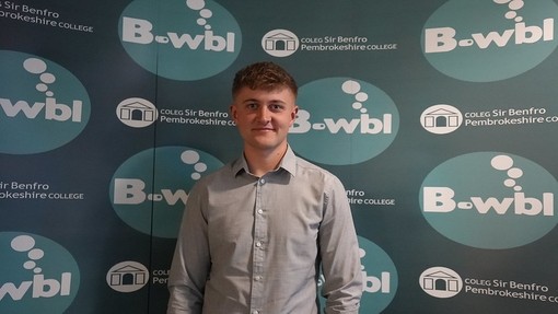 Owain in a shirt standing in front of Bwbl branding
