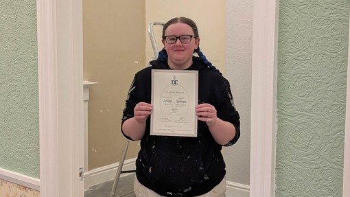 Bethan standing in a painting and decorating background holding her certificate at college