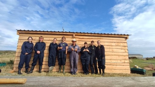 Lowri with a group in overalls outside a shed