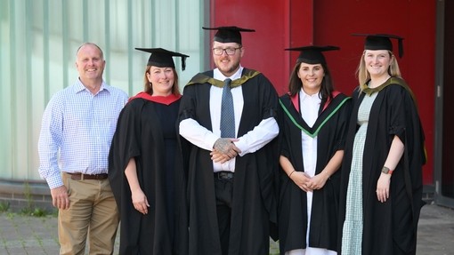 Keal standing in a line with his lecturers they are all wearing cap and gowns