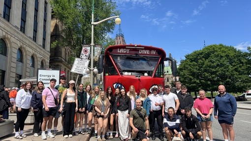 Students standing outside in a city by their red bus
