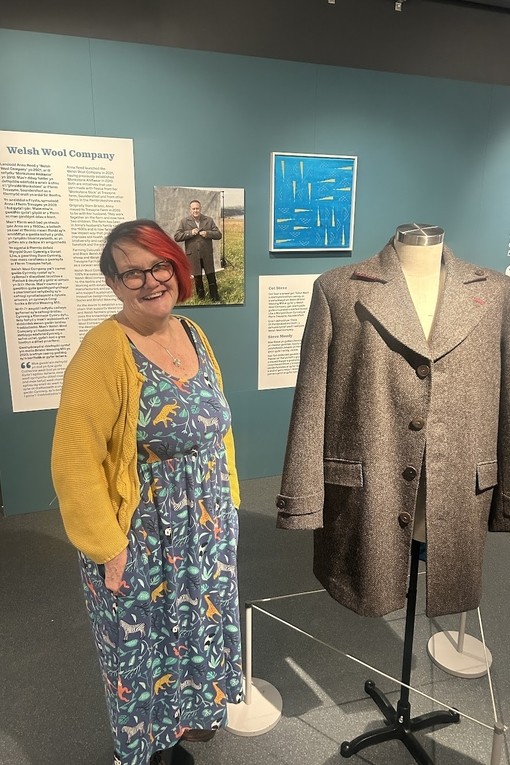 Allison in a mustard cardigan and dress standing next to the coat