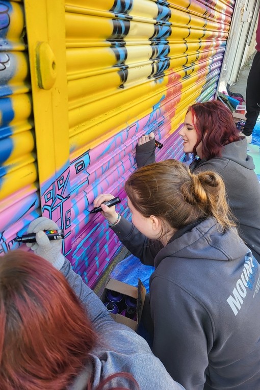 Students working on the shutters with bright coloured paint