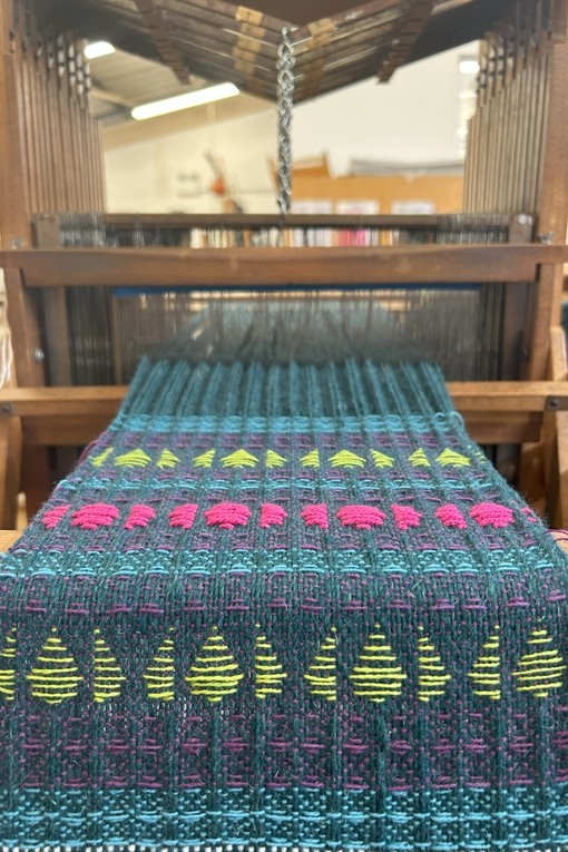 a piece of weaved material coming out of a weaving machine it's turquoise with pink and yellow