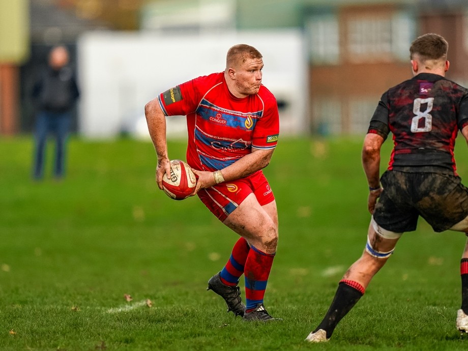 Student in red sports kit about to pass a rugby ball.