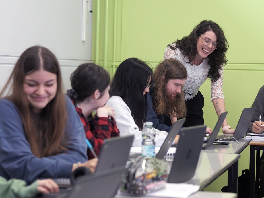 A group of smiling students in a classroom with a teacher leaning over them.