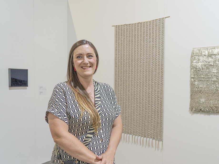 Laura Thomas stood in gallery in front of her artwork