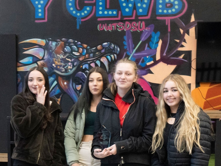 A group of students in front of a funky sign saying Y Clwb